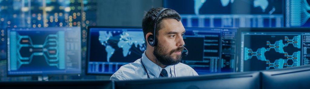 System Control Room Dispatcher Talks into Headset. He Controls Correct Work of the Facility. In the Background Multiple Monitors Show Technical Data. (System Control Room Dispatcher Talks into Headset. He Controls Correct Work of the Facility. In the